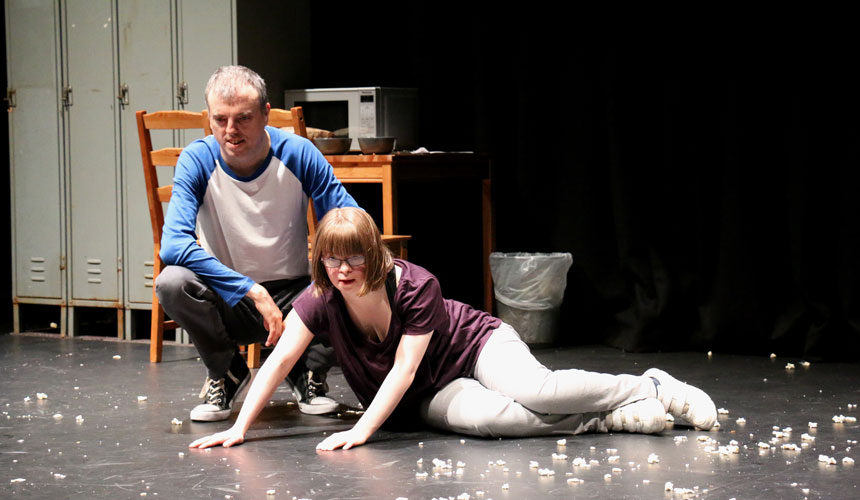 A woman laid on the floor with a man crouched to the side of her, waking her up