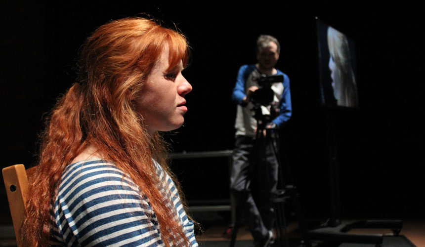 Side profile of a woman being filmed from a distance by a man.