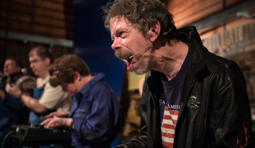 Jez Colborne in a black leather jacket sings in front of a band.