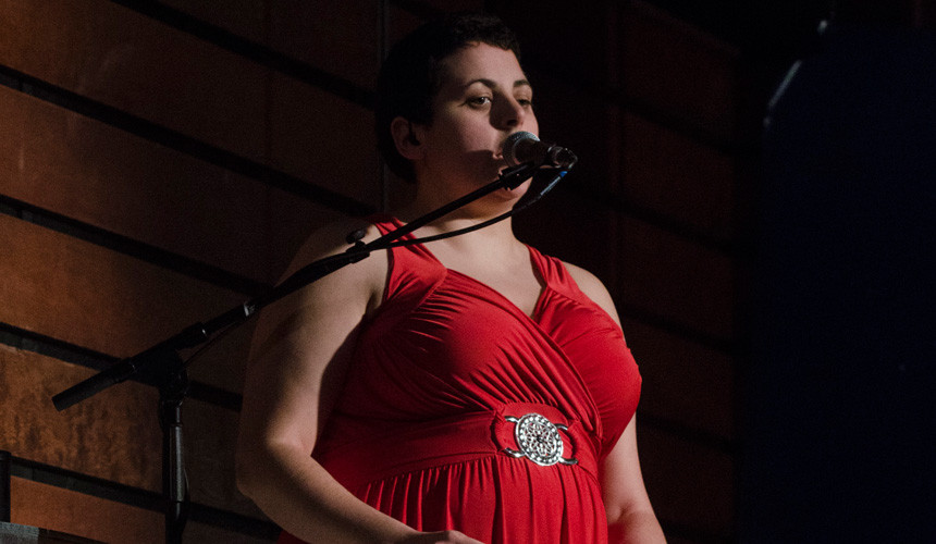 Elizabeth McCormack in a red dress with diamante buckle singing into a microphone.