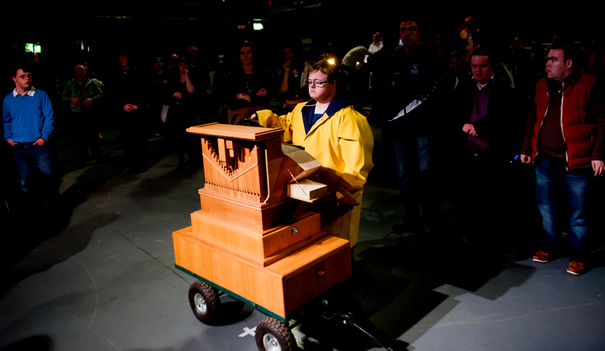 A man in yellow jacket playing a barrel organ